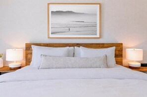 Un lit bien fait, avec du linge de lit blanc, une tête de lit en bois et deux lampes de chevet.