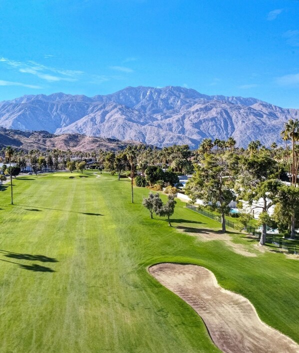 Un campo de golf con montañas al fondo, césped cuidado y palmeras.