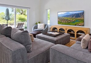 Een moderne woonkamer met een grijze modulaire bank, een houten salontafel en een grote flatscreen televisie aan de muur.