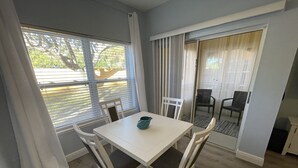 En matplats med ett vitt bord och stolar, en turkos kanna och en skjutdörr i glas som leder ut till en uteplats.