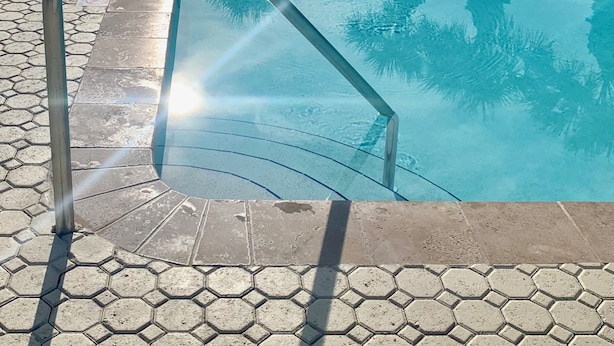 En swimmingpool med en metallstege och sexkantiga plattor runt om.