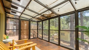 A sunroom with large windows, wooden furniture, and a view of the surrounding forest. - 1Br Hidden Gem overlooking Wetland Dog Friendly (Flagstaff)