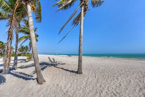 Ein Strand mit Palmen, blauem Himmel und ruhigem Meer.