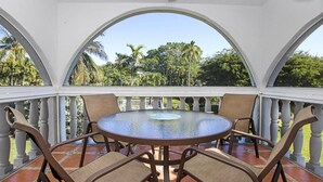 A covered outdoor seating area with a round table and chairs, surrounded by a white balustrade.
