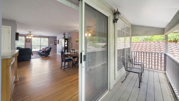 Een ruime woonkamer met houten vloer, een eethoek met tafel en stoelen, en een balkon met railing en uitzicht.