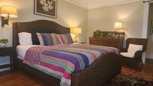 Camera luminosa con un letto grande, due lampade da comodino, un comodino, una cassettiera in legno, una sedia e un quadro appeso al muro.