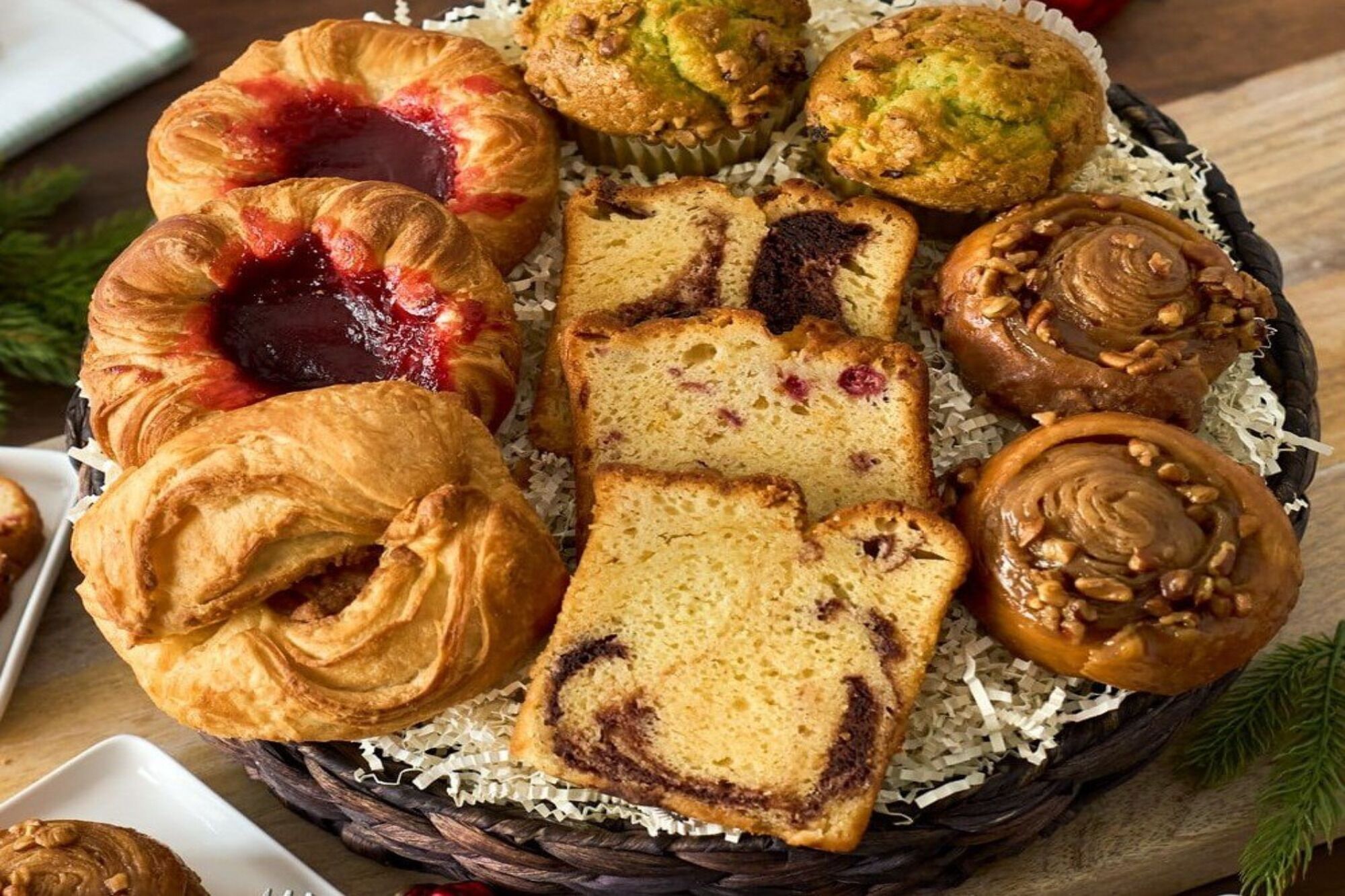 A basket of assorted pastries including croissants, muffins, and a slice of cake.