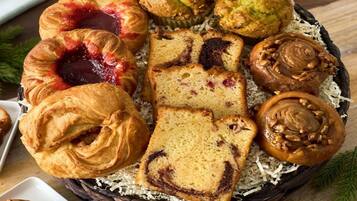 A basket of assorted pastries including croissants, muffins, and a slice of cake.