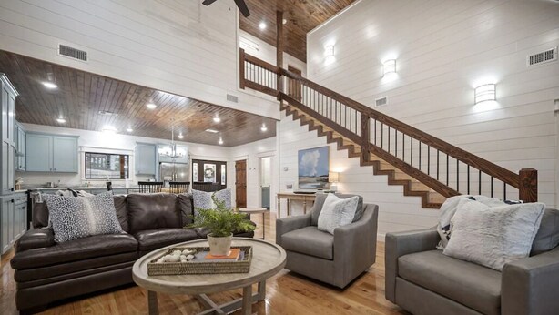 A spacious living area with a wooden staircase, leather sofas, and a round coffee table. - 3 Masters, w/Bunk Room, Shuffle Board, Arcades, Hot Tub-Great For Families (Broken Bow)