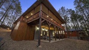 A two-story wooden cabin with a balcony, surrounded by trees. - 3 Masters, w/Bunk Room, Shuffle Board, Arcades, Hot Tub-Great For Families (Broken Bow)