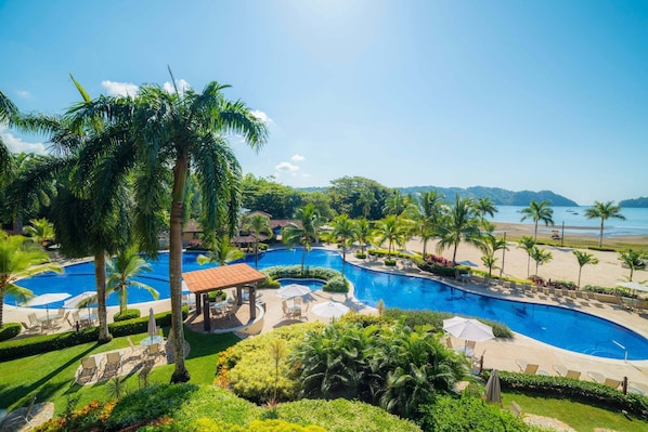 A resort with multiple swimming pools, palm trees, and a beach view.