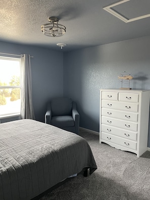 Une chambre à coucher avec un lit, une chaise, une commode et un ventilateur de plafond.