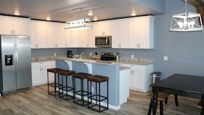 A modern kitchen with white cabinets, a stainless steel refrigerator, a microwave, and a bar area with stools.
