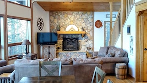 Ein gemütliches Wohnzimmer mit Kamin aus Stein, Holzboden und einem Essbereich mit großem Tisch und Stühlen.