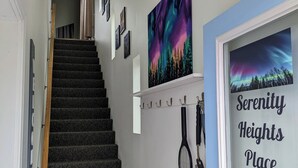 En gang med trappe, et indrammet billede af nordlys og en dør med skiltet "Serenity Heights Place".