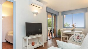 Una sala de estar moderna con una televisión de pantalla plana sobre un soporte blanco, un sofá y un comedor con una mesa y sillas.
