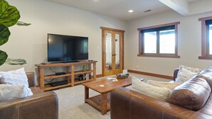 Un salón con televisor, mueble de madera para entretenimiento, sofá de cuero y un ventanal grande.