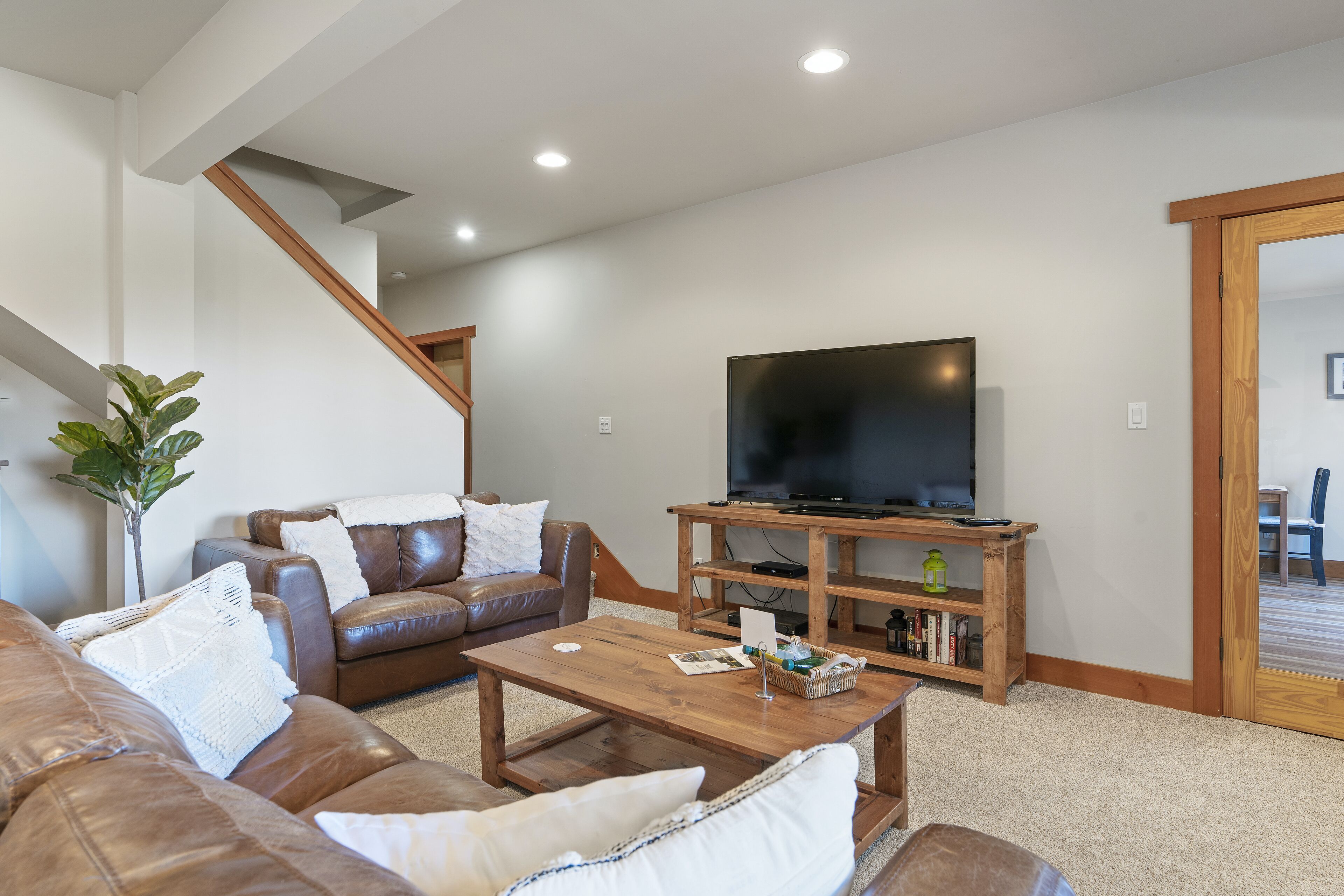 A living room with a brown leather sofa, a wooden coffee table, and a flat-screen TV on a wooden stand.