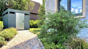 A pathway leading to a modern building with a brick facade and a window reflecting a clear sky.