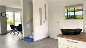 A modern interior with a staircase, a dining area with chairs, a kitchen counter, and a view through a window.
