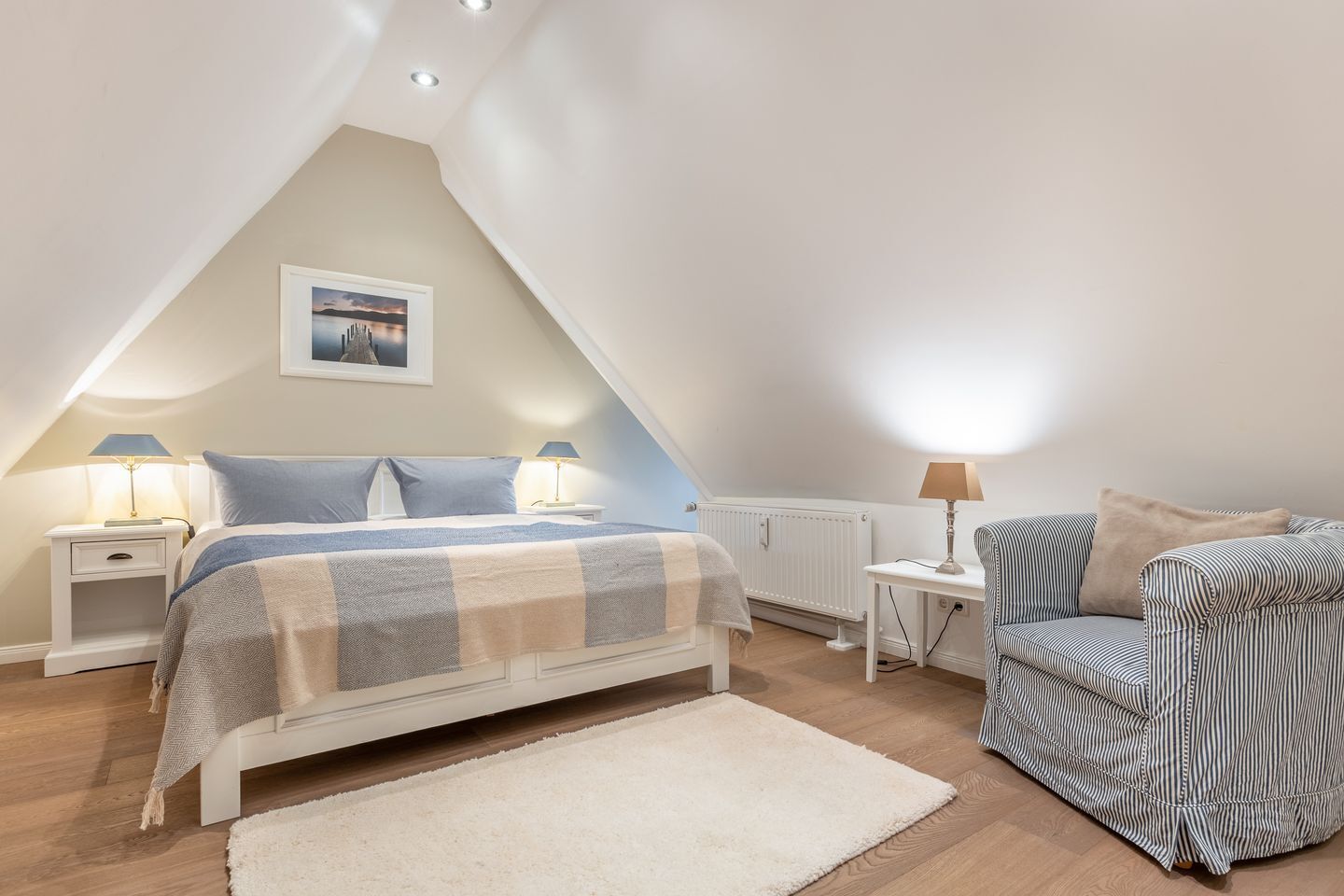 Ein Schlafzimmer mit einem Bett, Nachttischen, einem Sessel, einer Heizung und einem Bild an der Wand.