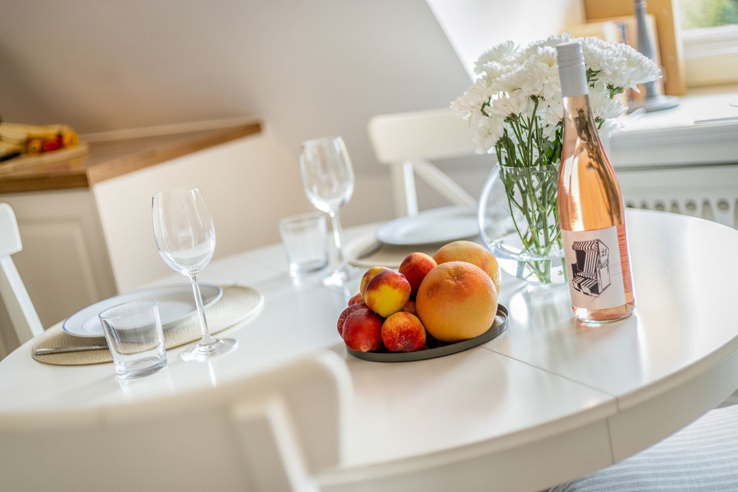 Une table à manger avec une assiette de fruits, une bouteille de vin et un vase de fleurs.