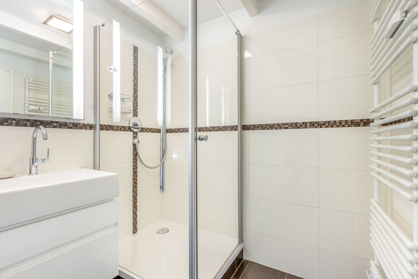 A modern bathroom with a glass-enclosed shower, a white sink with a chrome faucet, and a tiled floor.