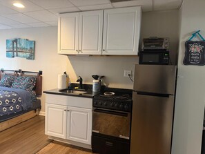 A compact kitchen with white cabinets, a stove, a refrigerator, and a microwave.