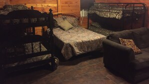 Ein blockhaushaltsähnliches Zimmer mit zwei Etagenbetten, einem Holz-Kopfteil, einem kleinen Sofa und einem Fliesenboden.