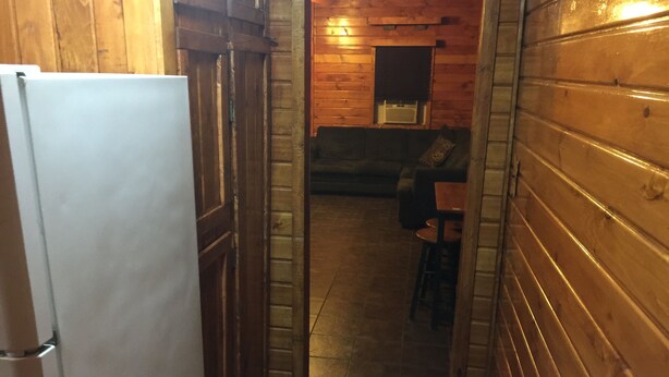 Ein schmaler Korridor mit Holzwänden und Fliesenboden führt zu einer Sitzecke mit Tisch und Stühlen.