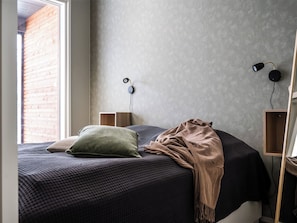 Une chambre à coucher avec un lit, des oreillers, une couverture, une lampe fixée au mur et un haut-parleur.