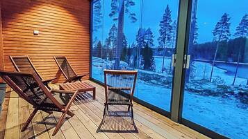 A wooden deck with three lounge chairs and a glass door leading to a snowy outdoor scene.