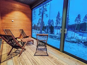 Een houten terras met drie loungestoelen en een glazen deur die uitkomt op een besneewd landschap.