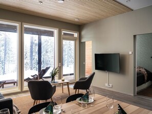 Un salon moderne doté d’un grand téléviseur, d’un espace salon et offrant une vue sur une forêt enneigée.