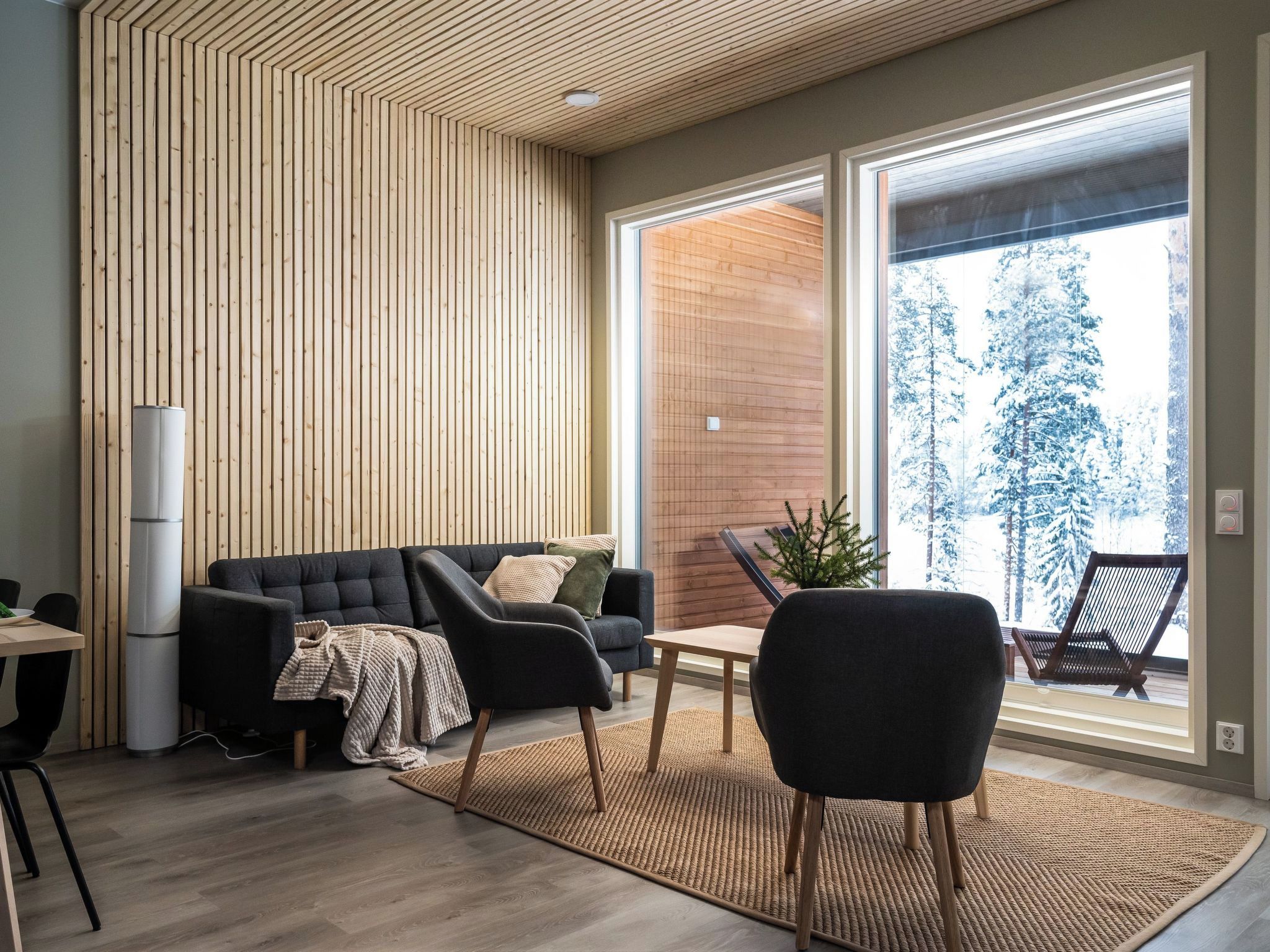 A modern living room with a sofa, chairs, a coffee table, and a large window with a view of snow-covered trees.