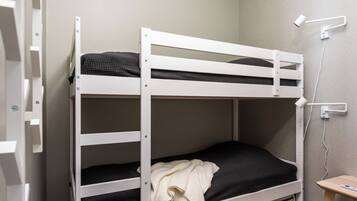 Una cama litera con estructura blanca, una mesita pequeña y un aplique de pared.