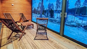 A wooden deck with two lounge chairs and a glass wall offering a view of a snowy landscape.
