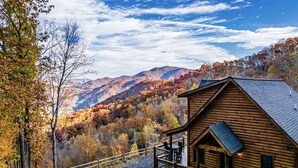 Eine Holzhütte mit einer Terrasse und Blick auf herbstlich gefärbte Bäume und Berge.