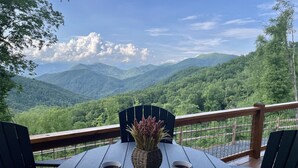 Ein runder Tisch mit zwei Stühlen, einer Speiseplatte und zwei Kaffeetassen auf einer Terrasse mit Blick auf grüne Berge.