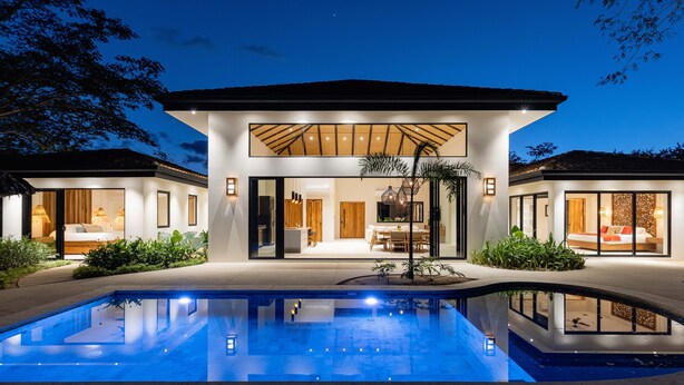 Une maison moderne à deux étages, dotée d’une piscine, de grandes fenêtres et d’un intérieur bien éclairé.