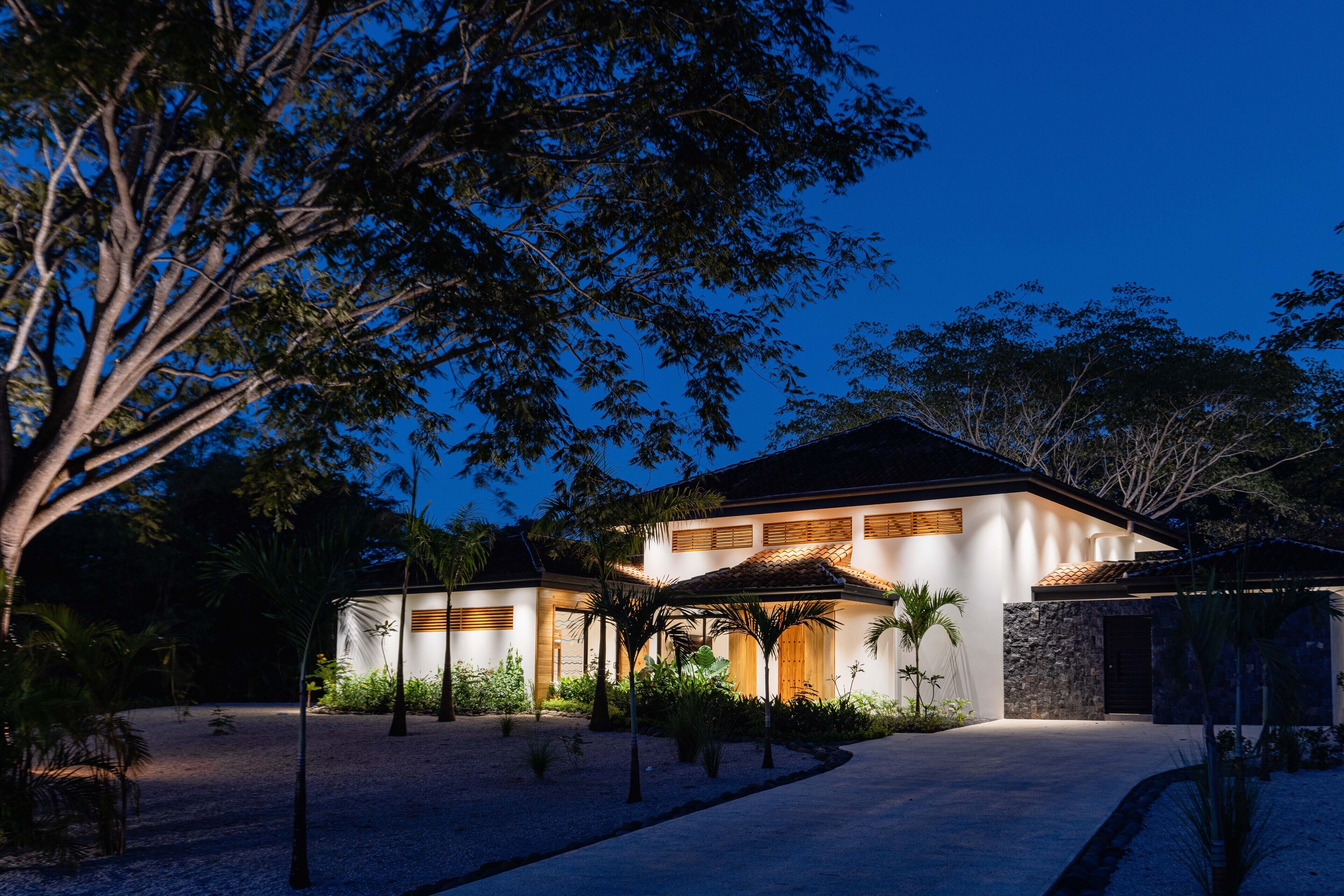Una casa moderna con un amplio camino de entrada, rodeada de palmeras y un jardín bien cuidado.