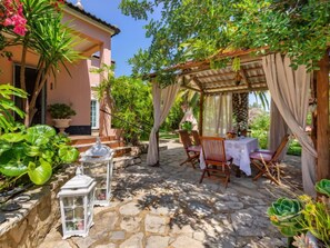 Une terrasse en pierre agrémentée d’une pergola, de coins salon extérieurs et d’une végétation luxuriante.