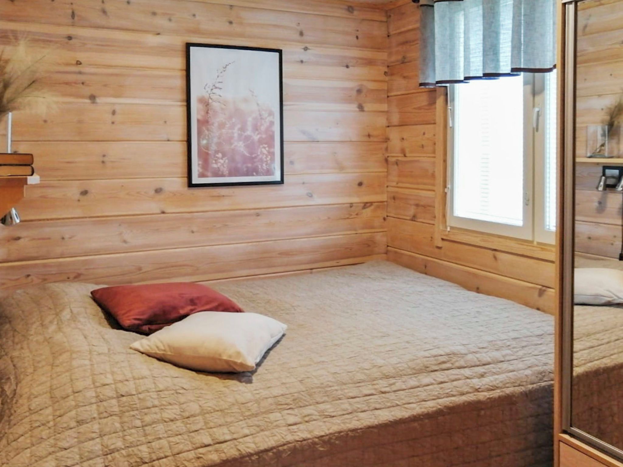 Een kamer met een bed, een ingelijst schilderij aan de muur en een raam met gordijnen.