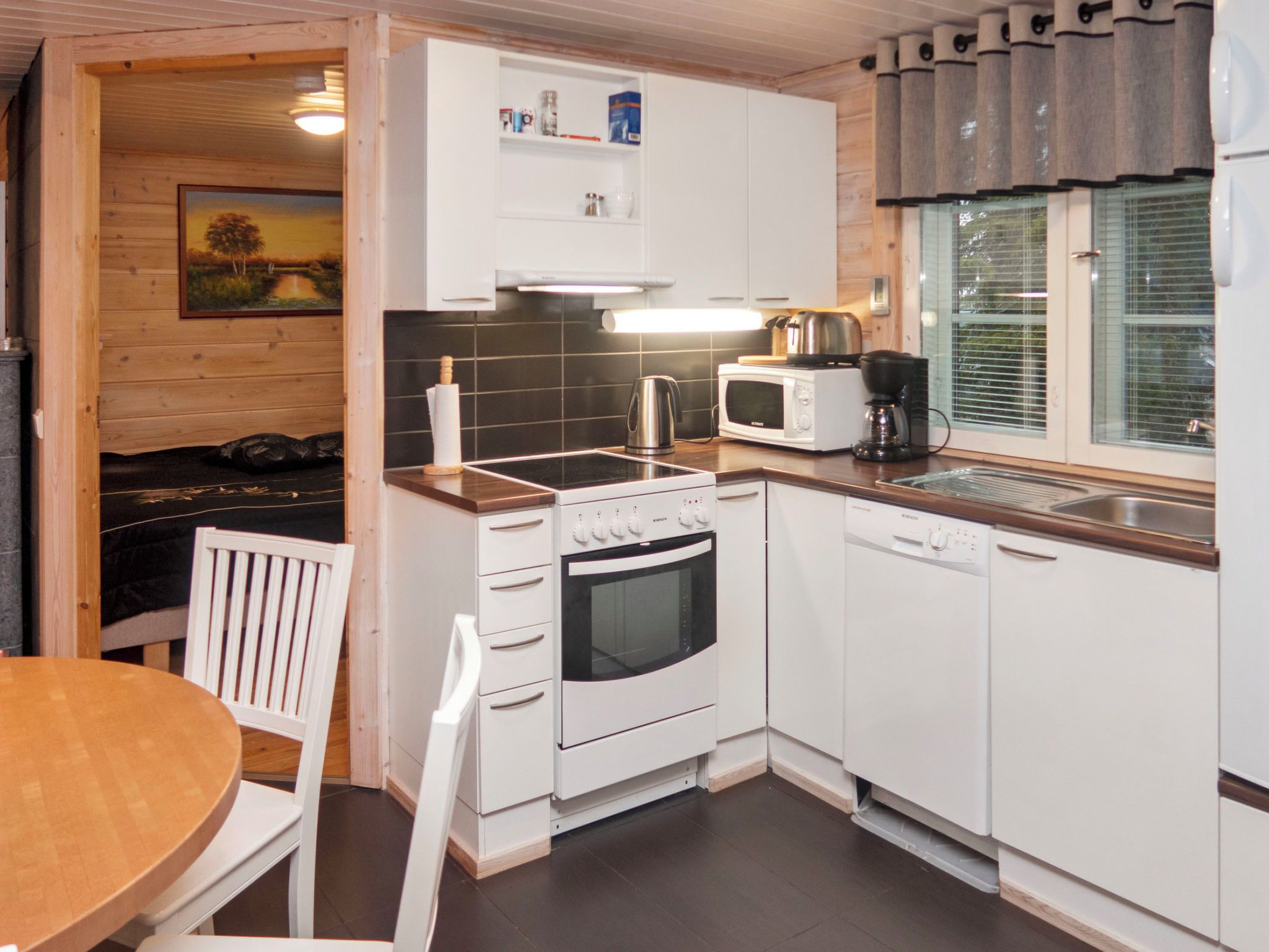 Cocina compacta con estufa, horno, microondas y un pequeño comedor con mesa y sillas.