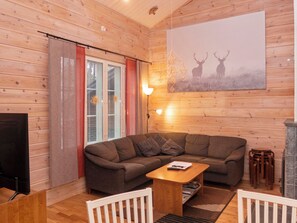 En hyggelig stue med træpaneler, en sofa, et sofabord, en pejs og et billedkunstværk med dådyr på væggen.