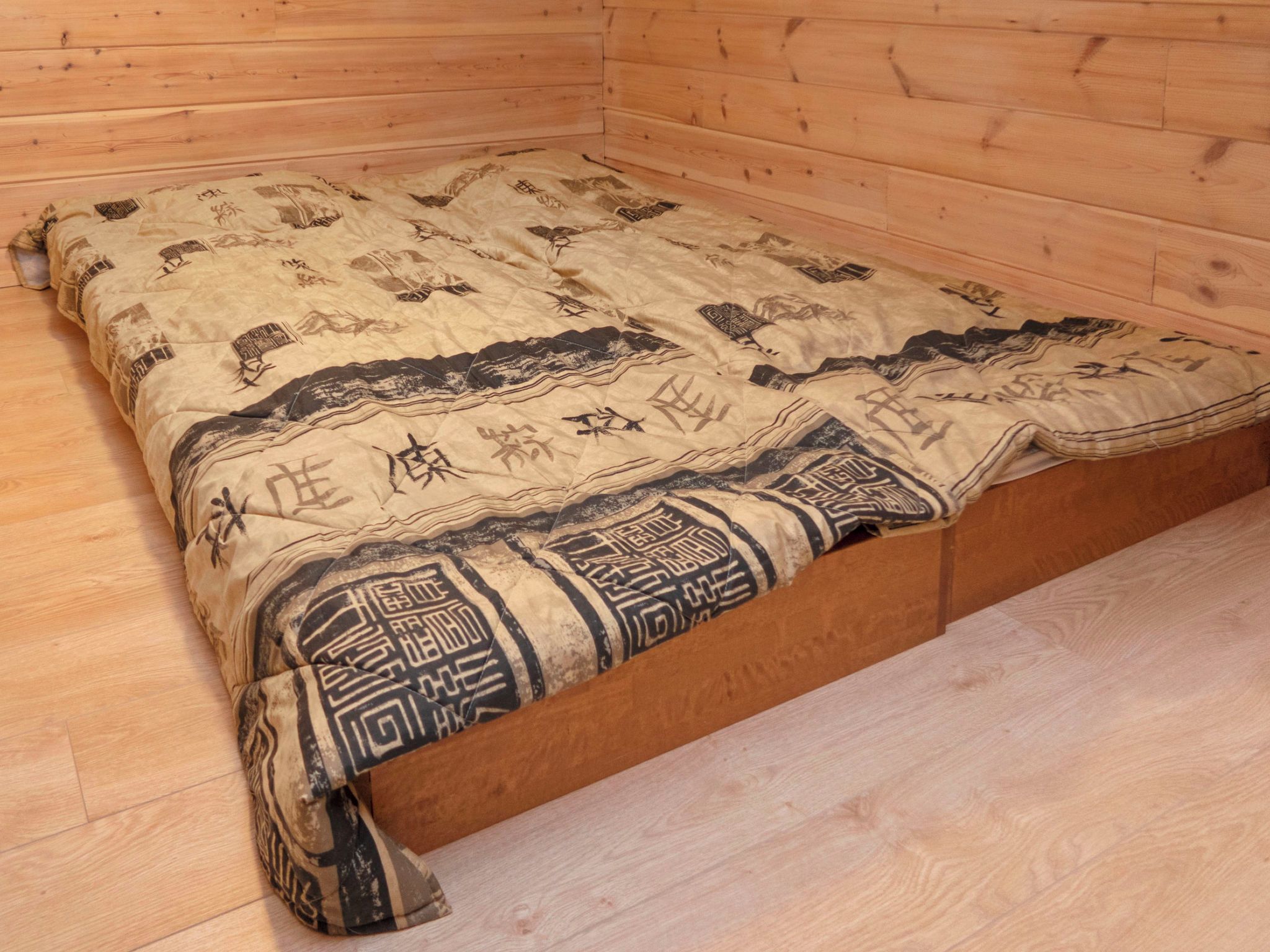 A wooden room with a bed, a wooden floor, and a wall with a wooden panel.