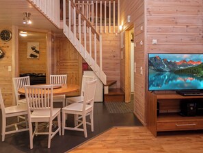 A wooden interior with a dining area, a staircase, and a television displaying a mountain landscape.