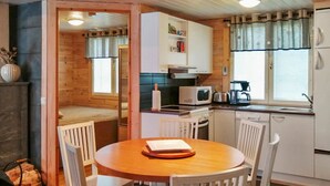 A cozy kitchen with a round wooden table and white chairs, a microwave, a coffee maker, and a window with curtains.