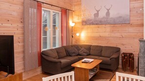 A cozy cabin interior with a sectional sofa, a small wooden table, a fireplace, and a wall-mounted artwork of deer.