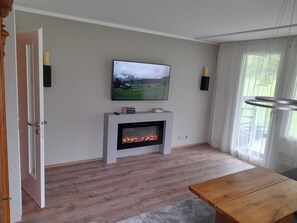 A living room with a fireplace, a television mounted on the wall, and a wooden table.